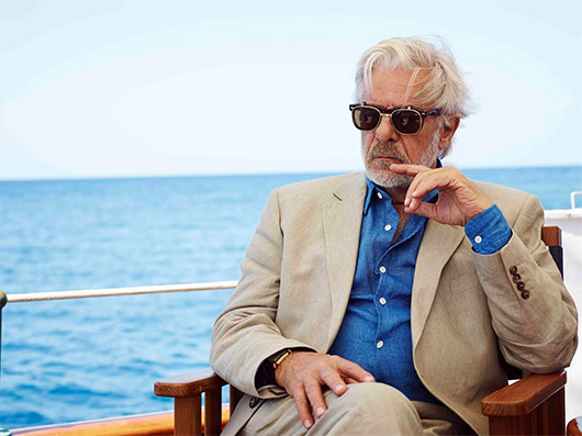 Giancarlo Giannini wearing sunglasses and sitting in front of a body of water, with Johnnie Walker and Actor
