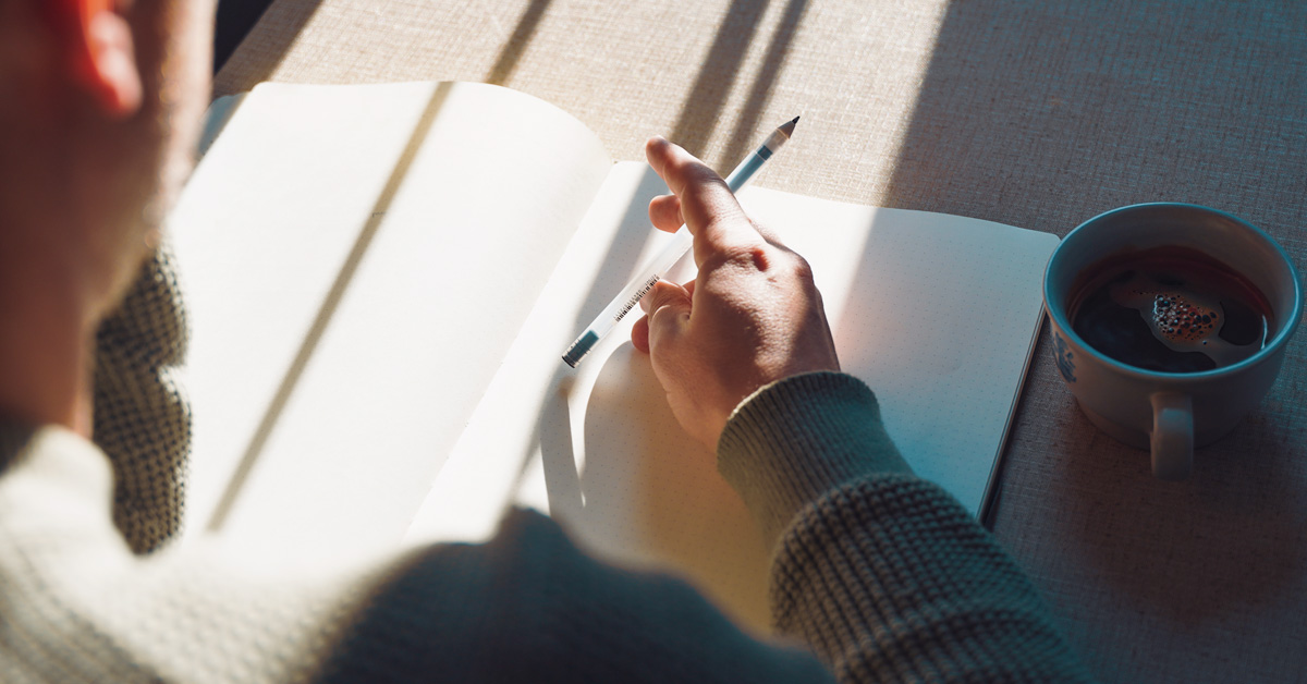 Journaling_wide over the shoulder shot of a person journaling with. sun streaming in through a window