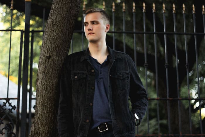 A person standing in front of a fence, with Stacy Man wearing black trucker jacket with blue henley