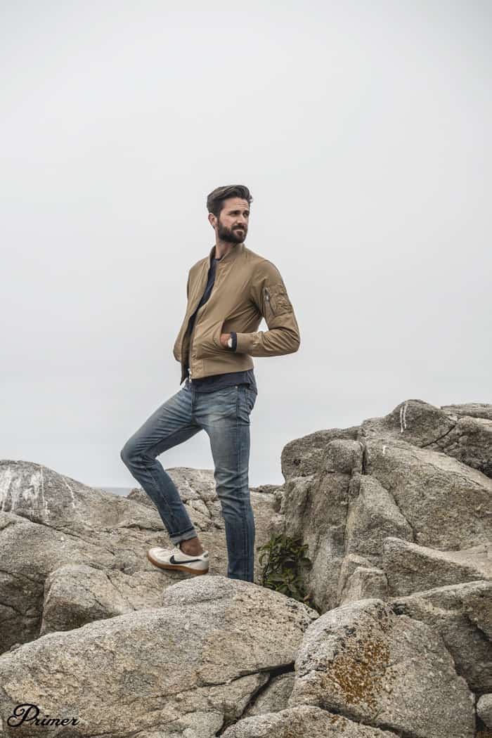 man wearing tan bomber jacket standing on rocks