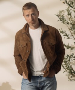 man wearing a suede trucker style jacket over a crew neck shirt and denim jeans