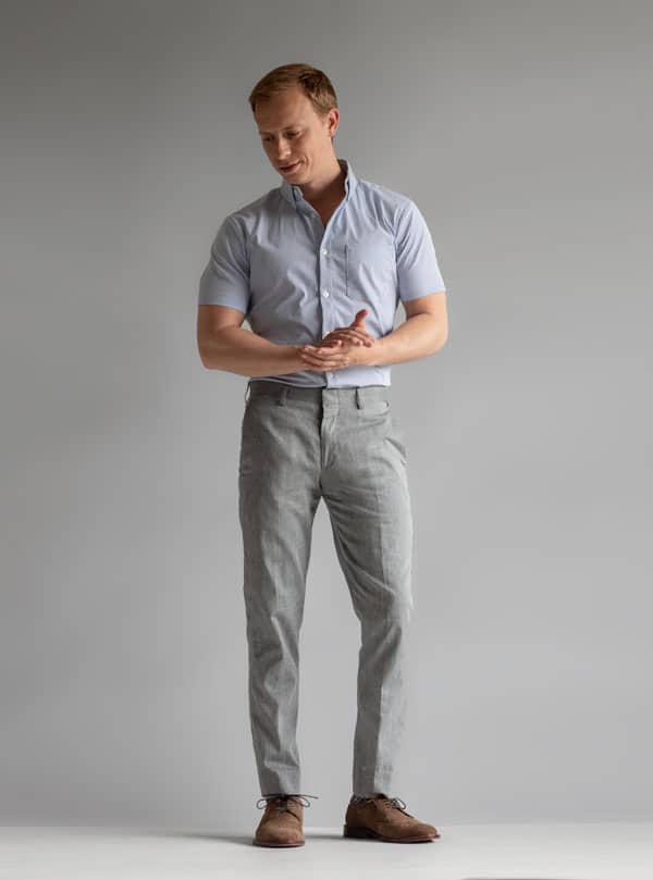 A man standing in front of a wall wearing gray pants and a short sleeve shirt