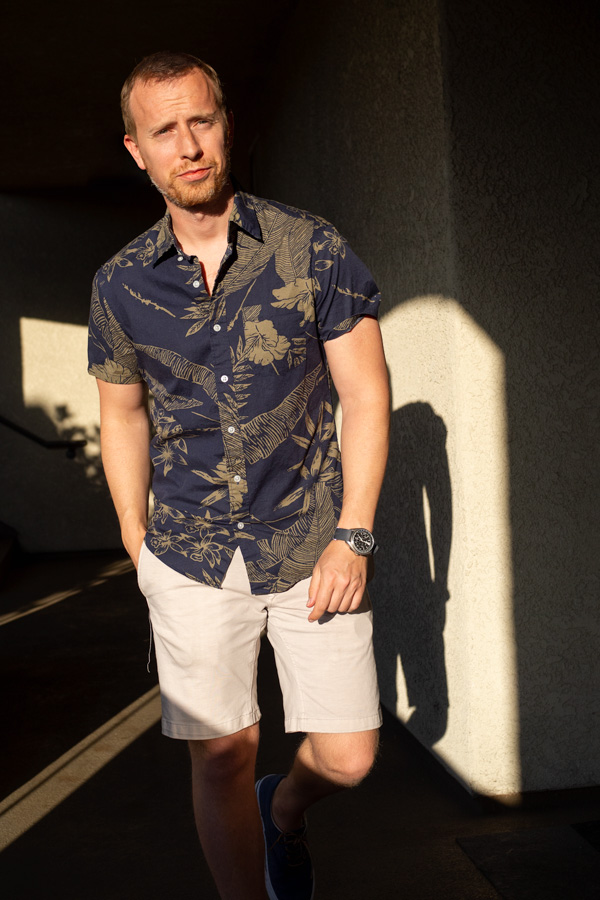 A person standing posing for the camera with a floral short sleeve shirt
