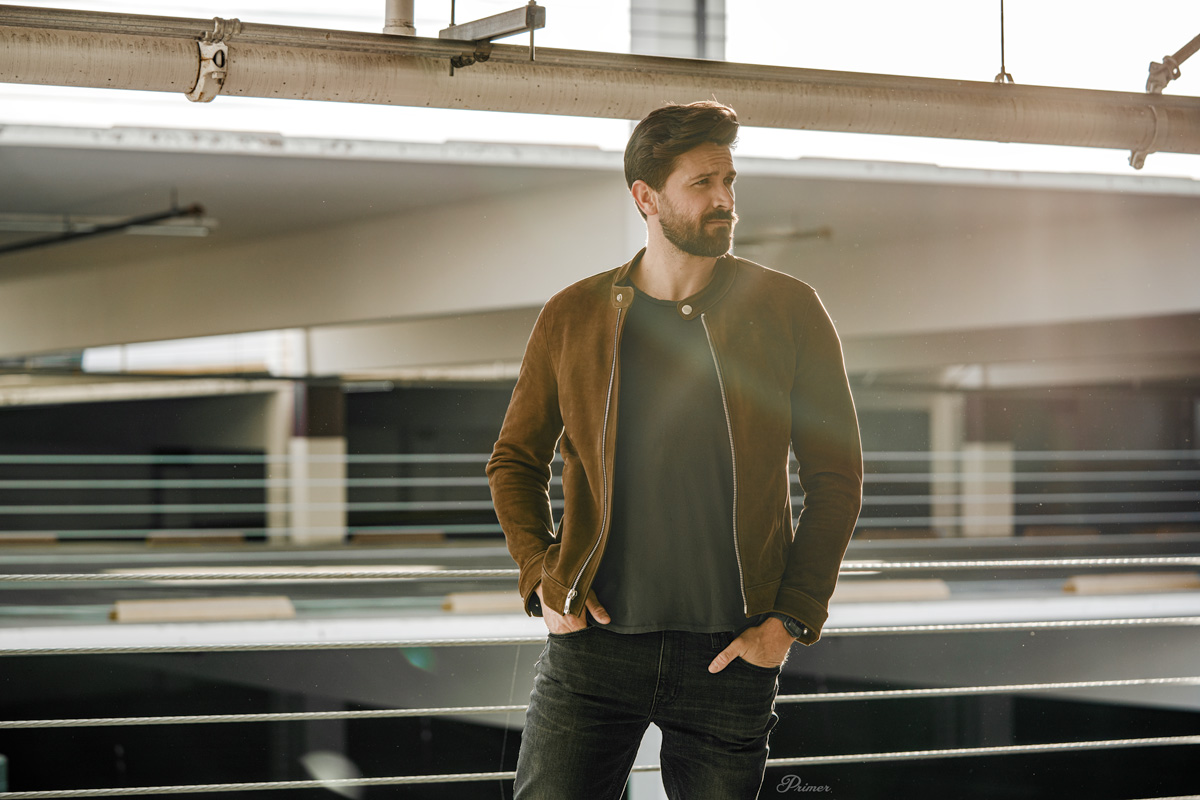 man wearing brown leather racer jacket with gray tshirt and jeans