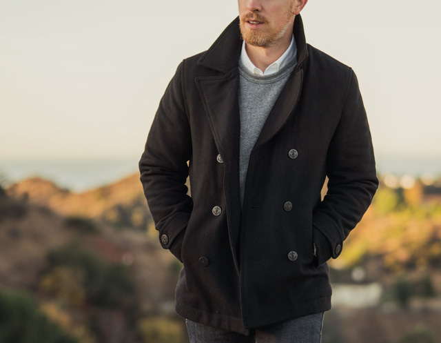 Man wearing black pea coat with gray sweatshirt and white oxford cloth button down