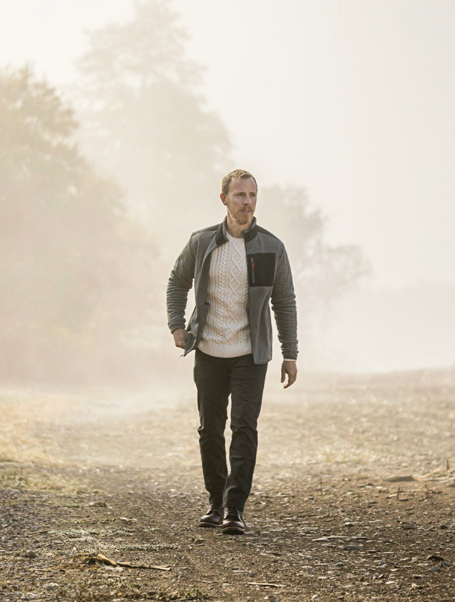 a man wearing a fleece jacket, knit sweater, pants, and boots