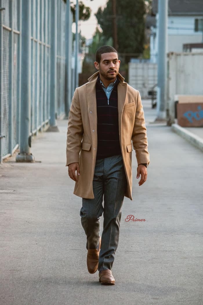 a man wearing a overcoat over a half zip sweater, pants, and dress shoes