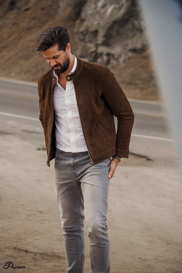 a man wearing a suede jacket over an oxford shirt and jeans
