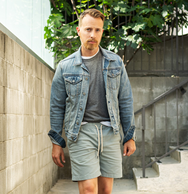 man wearing light blue denim trucker jacket with gray t-shirt and green drawstring shorts in summer