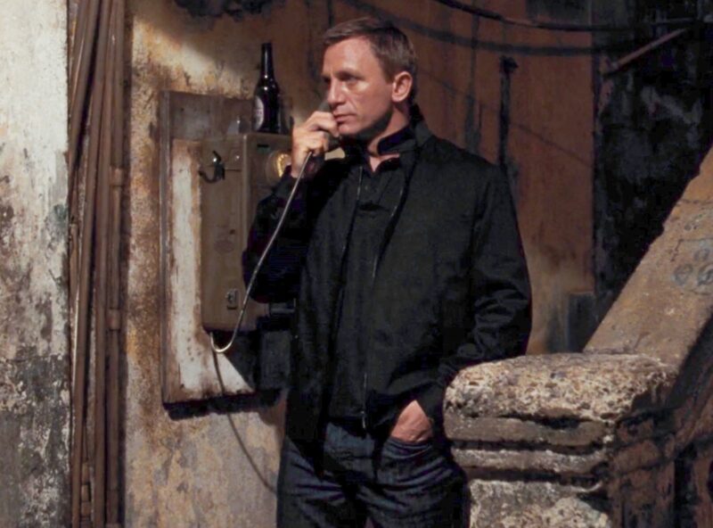 daniel craig james bond wearing a dark harrington jacket and using a telephone receiver