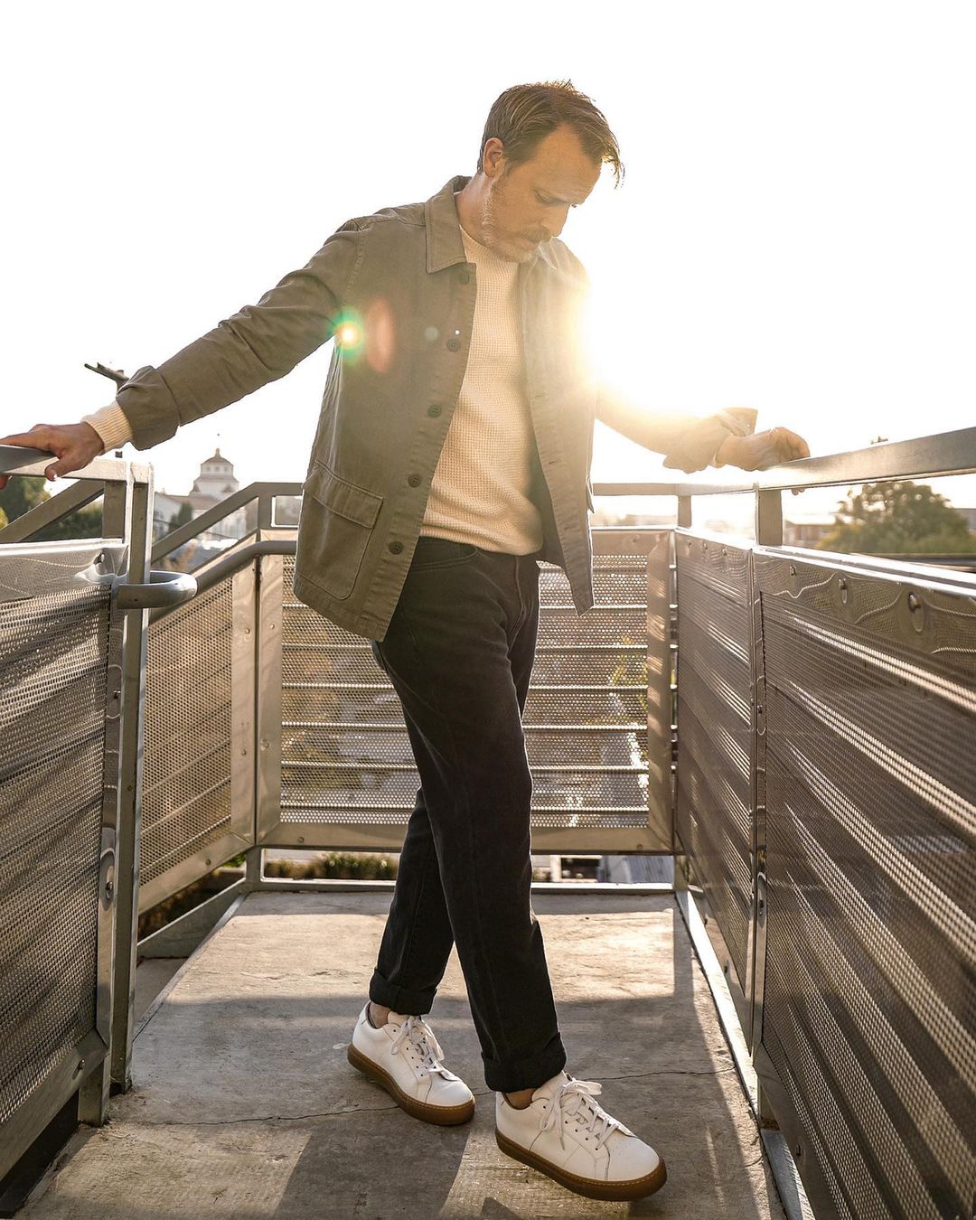 a man wearing a chore jacket over a sweater with jeans and gum sole sneakers