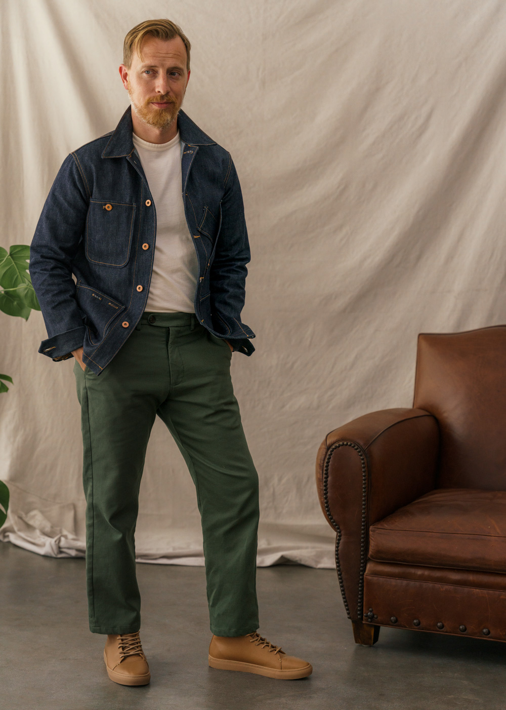 man wearing a denim tellason chore coat with white oxford shirt, green og 107 pants and red wing boots