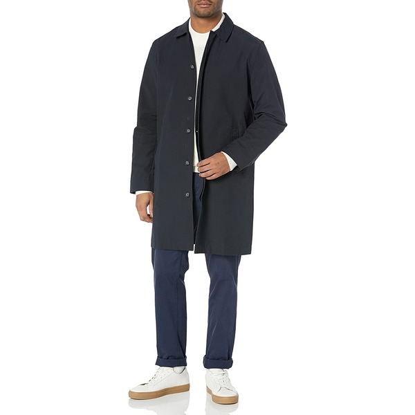 a man wearing a long black coat over fitted pants and white shoes