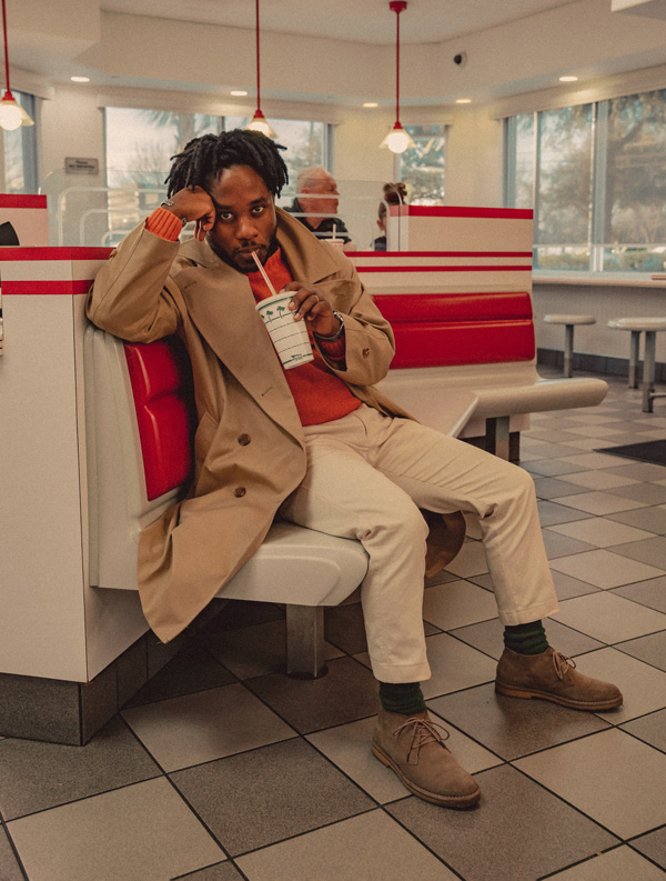 man wearing a trench coat outfit with a sweater, khakis, and suede boots