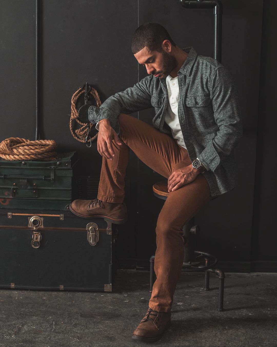 a man wearing khaki pants with boots and an unbuttoned overshirt