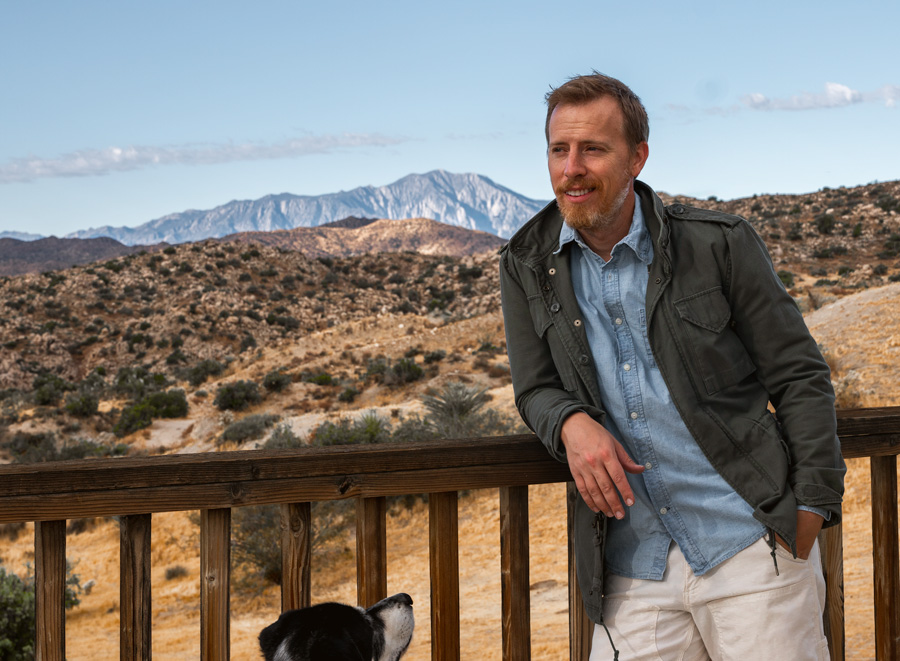 mens fall outfit with a chambray shirt, olive green jacket and white pants in the desert