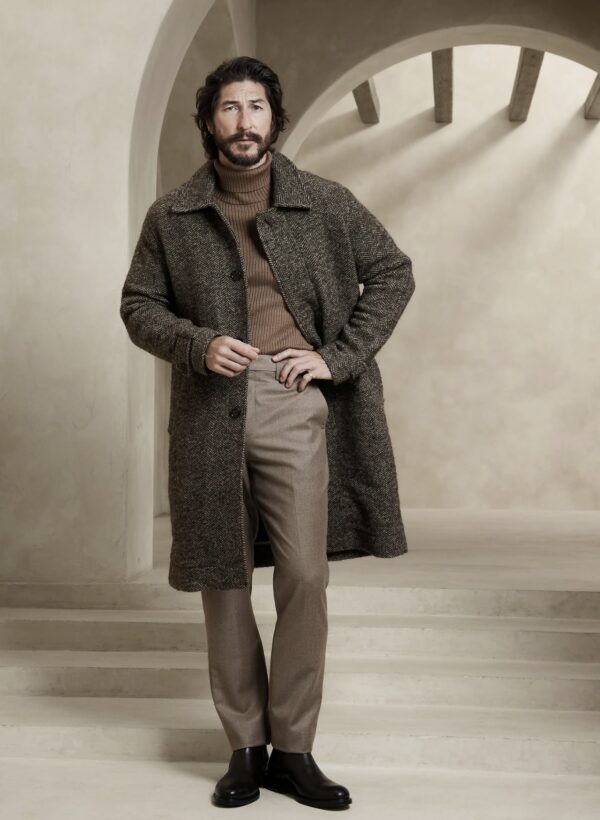 man wearing a car coat over a turtle neck sweater and trousers