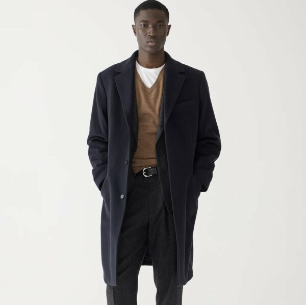 a man wearing a topcoat over a sweater and pants