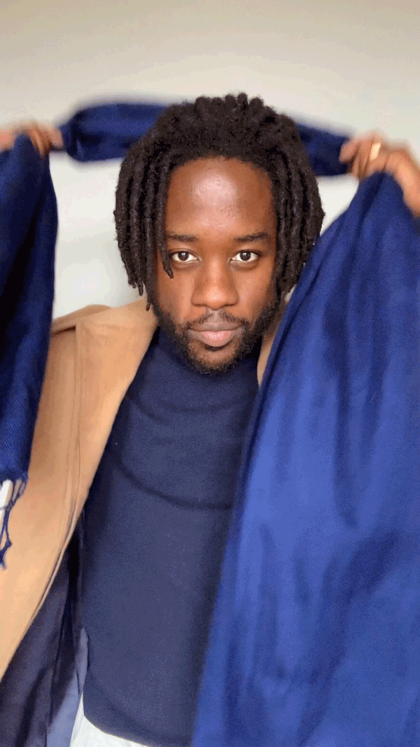 A man places a scarf behind his neck and drapes the tails in front of him untied.