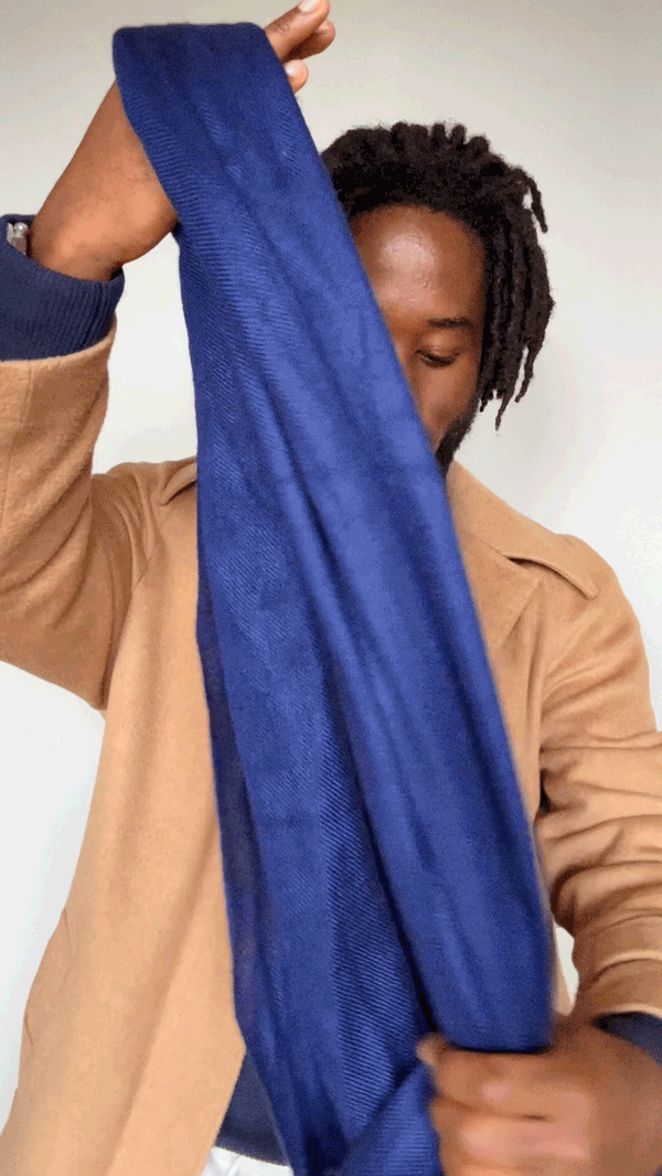 man tying parsian scarf knot: he folds it in half, wraps it around his neck passing the two ends through the loop made where it is folded and adjusts the front