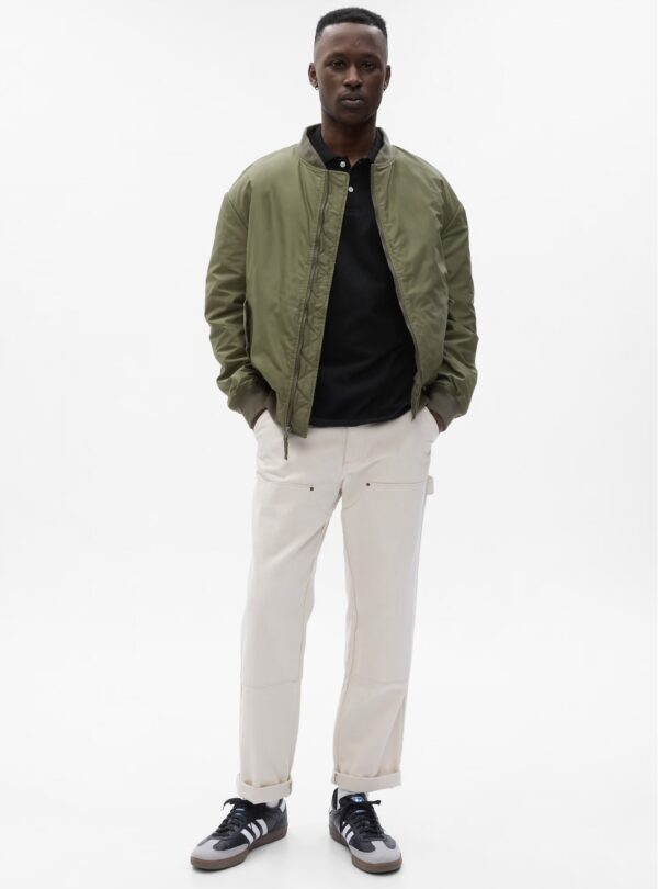 a man wearing a zip front bomber jacket over a shirt and slim fit pants