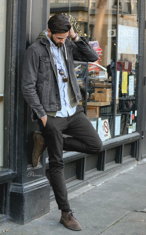 a man wearing a jean jacket over unzipped hoodie button front shirt slim pants and boots