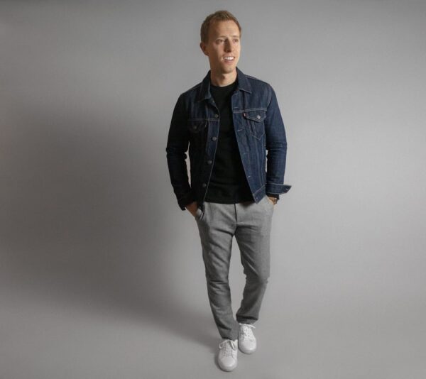 a man wearing a jean jacket over a crew neck sweater with slim fit pants and casual sneakers