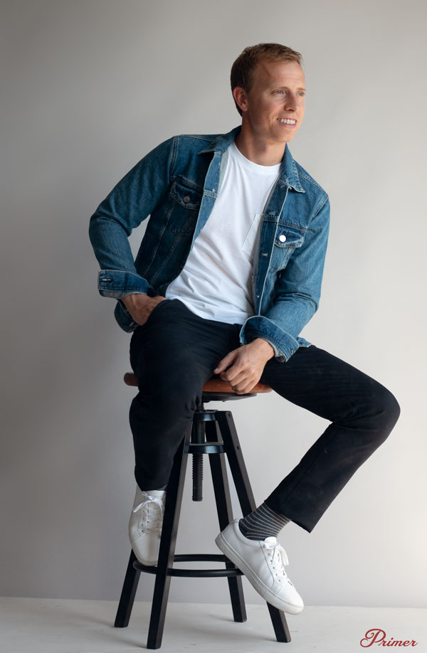 a man wearing a jean jacket over a crew neck casual shirt slim fit pants and casual shoes