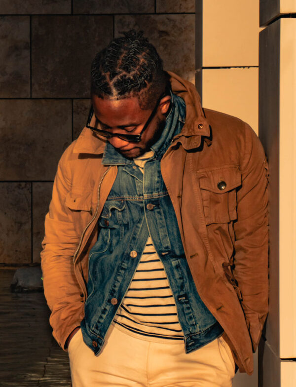 a man wearing a field jacket layered over a jean jacket and striped shirt