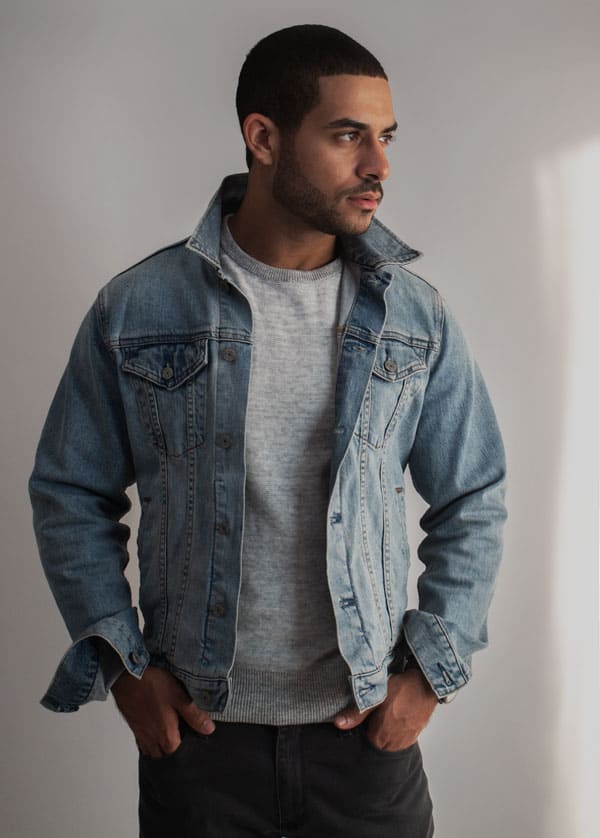 a man wearing a light wash jean jacket over a casual crew neck shirt