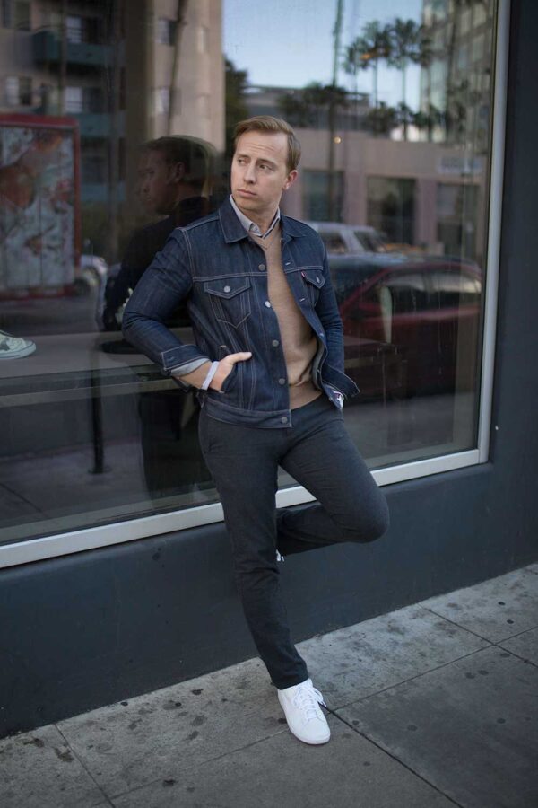 a man wearing a jean jacket over a sweater slim fit pants and casual sneakers