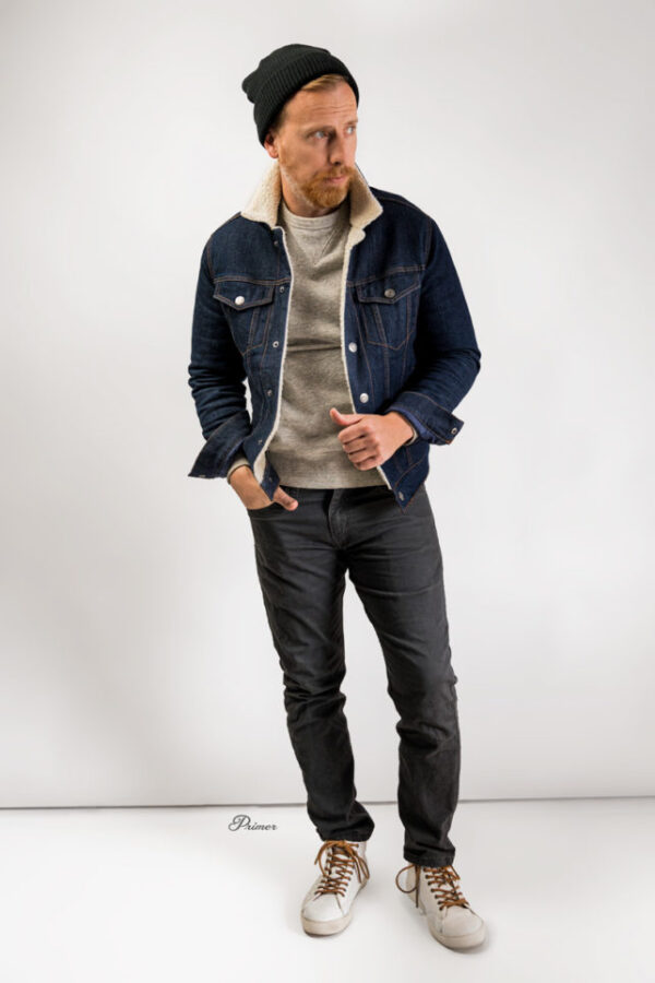 a man wearing a sherpa lined jean jacket with a sweater slim fit jeans and a beanie hat