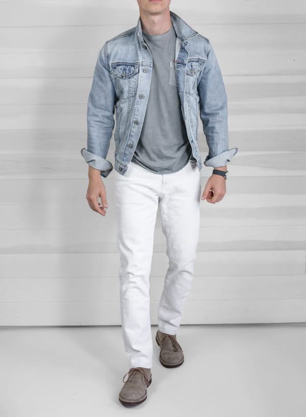 a man wearing a light wash jean jacket over a shirt slim fit white pants and boots