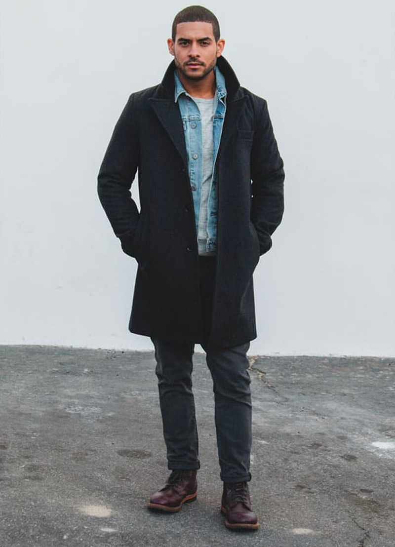 man wearing a top coat over a jean jacket with gray jeans