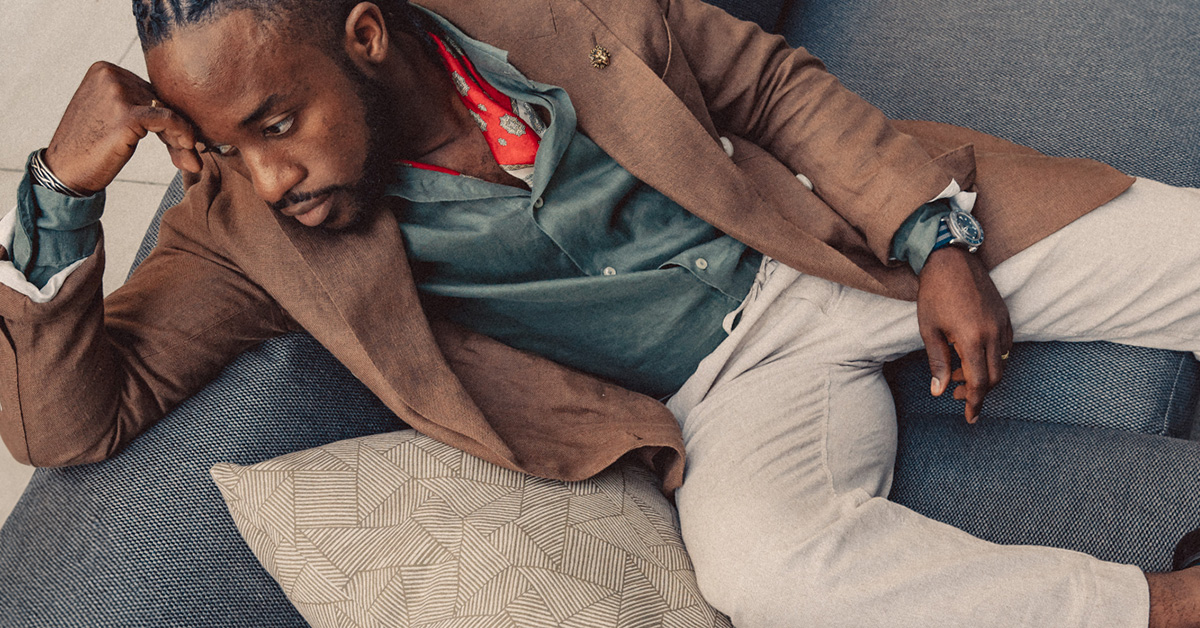 A man wearing linen pull on pants with a linen shirt and linen blazer, laying on a couch