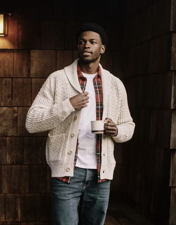 a man wearing a cardigan sweater layered over a flannel shirt and denim jeans