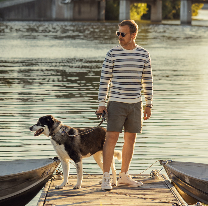 andrew with his dog leela standing on a dock while he wears shorts with converse high top sneakers