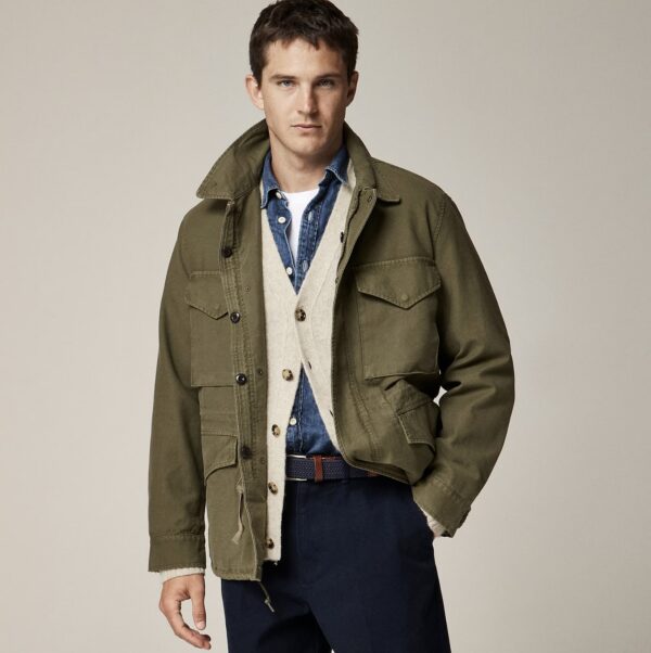 a man wearing a field jacket layered over a sweater and shirt with pants