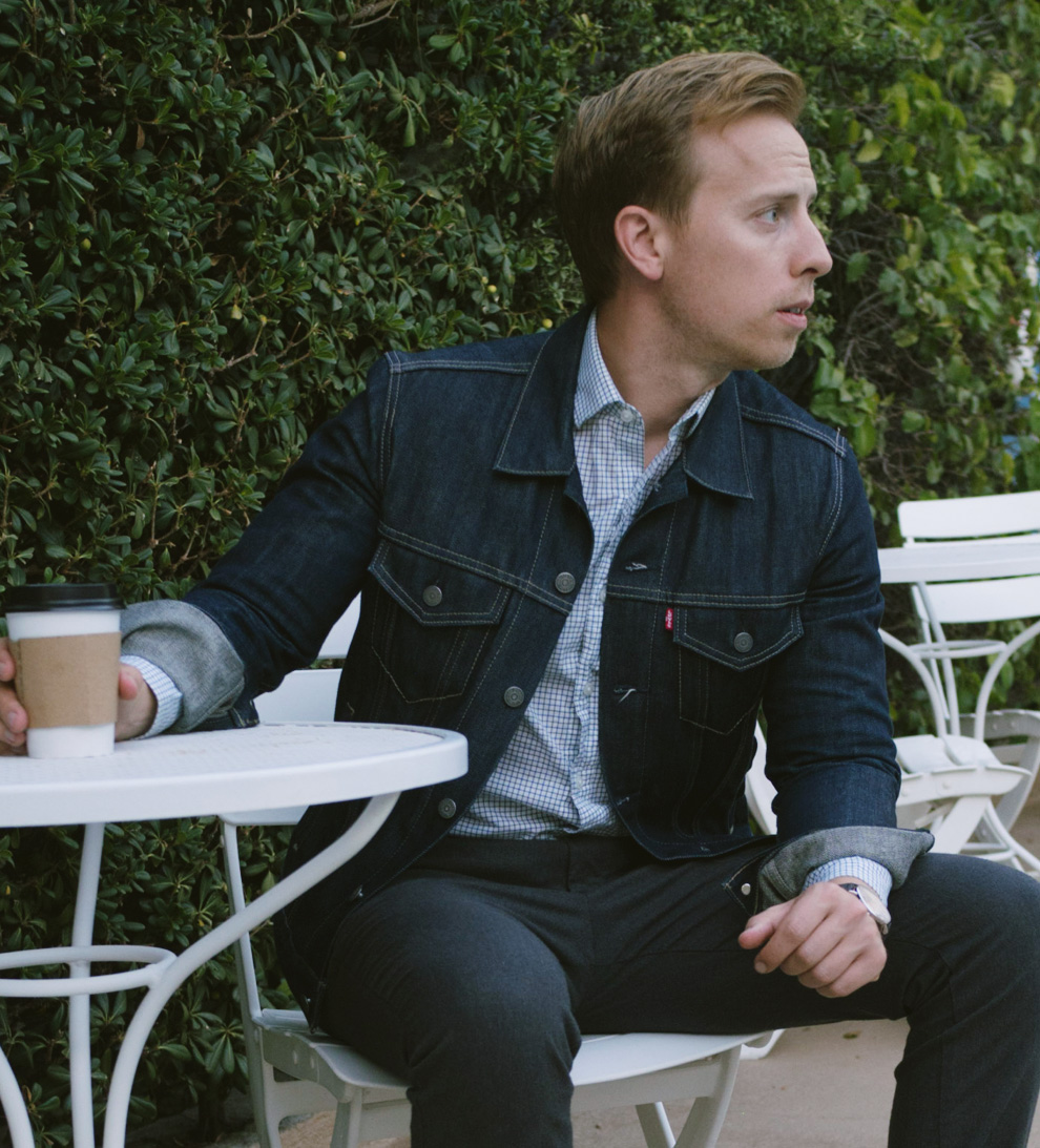 a man wearing a jean jacket over a dress shirt slim fit pants and dress boots