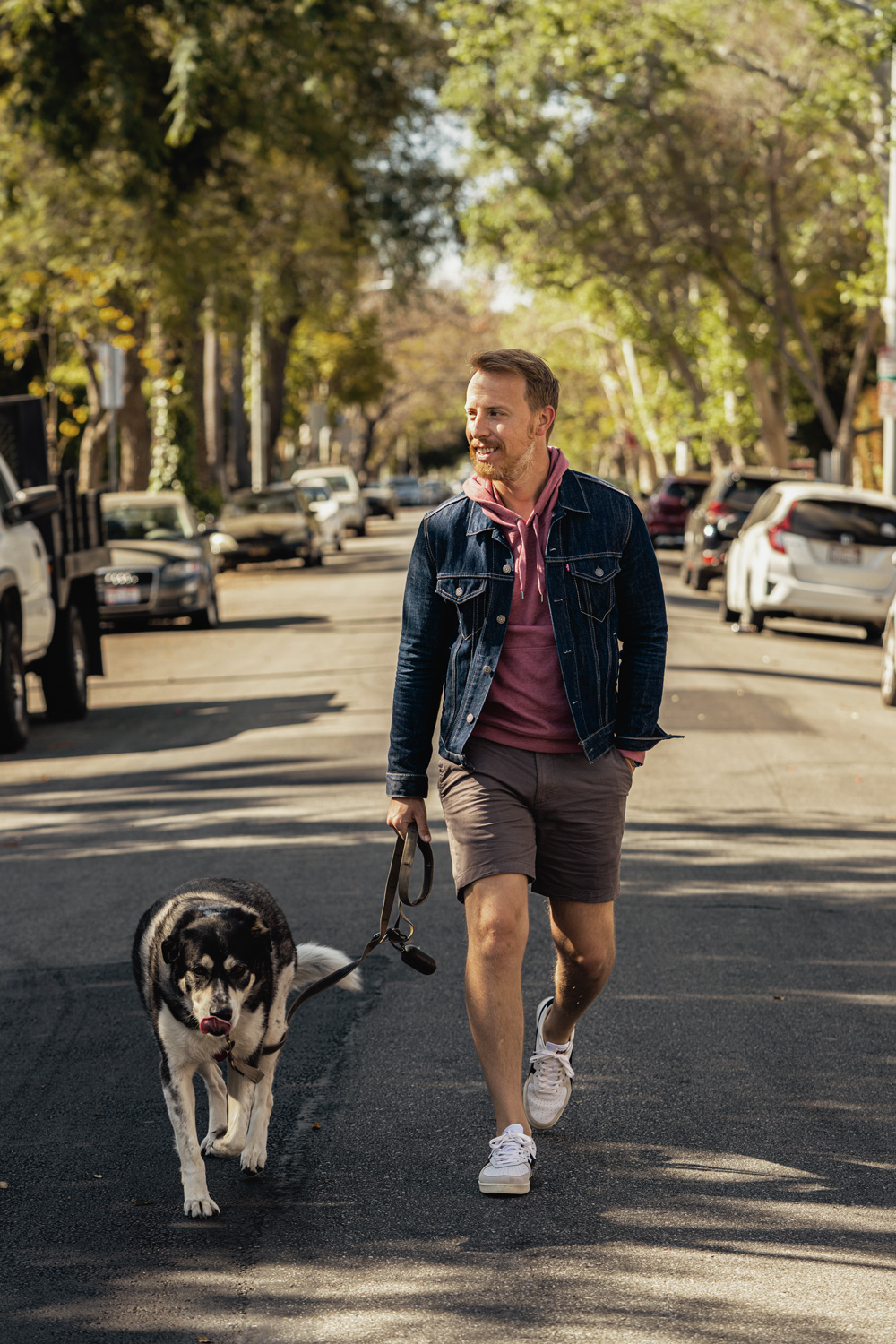 andrew walking leela while wearing a denim jacket with shorts and a red hoodie