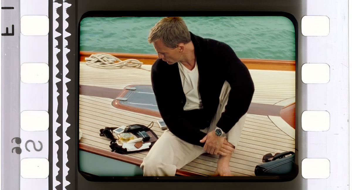 frame still of james bond wearing a cardigan white tshirt and tan chinos on a boat in casino royale