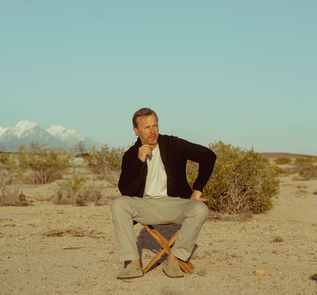 a men's fall outfit featuring a black cardigan sweater, white pocket t-shirt, and tan chino pants with suede birkenstocks