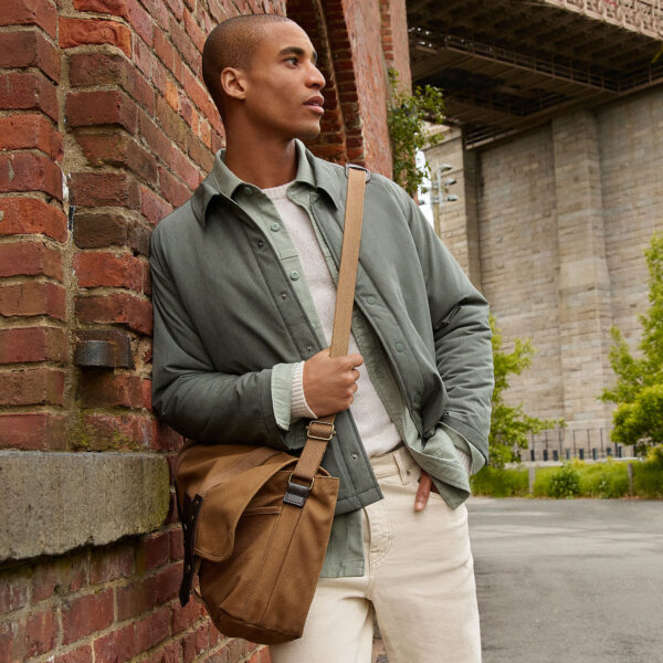 man wearing an insulated shirt jacket over a sweater and pants and carrying a messenger style bag