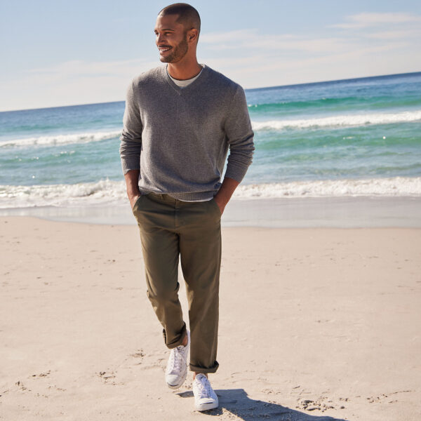 a man wearing chino pants with a sweater and casual shoes and taking a walk on a beach