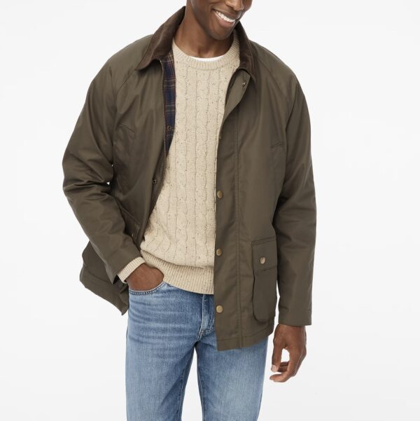 a man wearing a waxed twill jacket over a cable knit sweater and denim jeans
