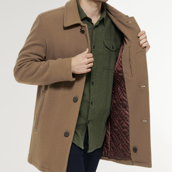 a man wearing a car coat over a button front shirt and pants