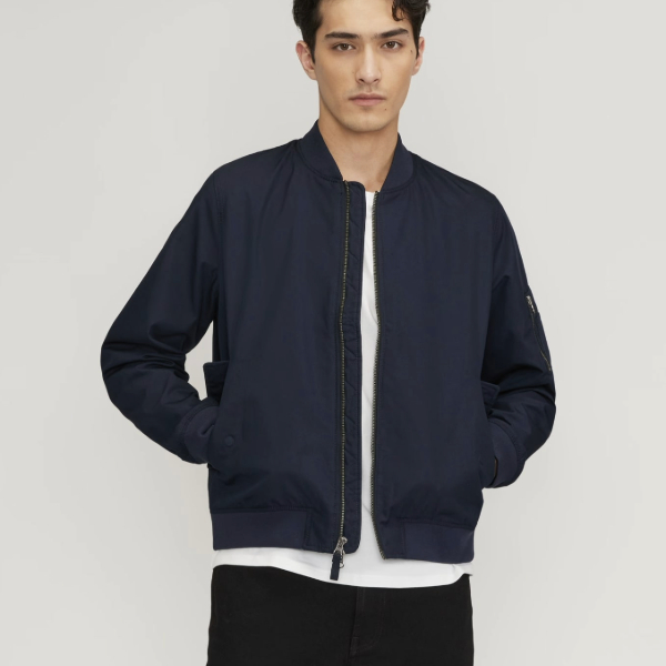 a man wearing a bomber style jacket over a shirt and pants