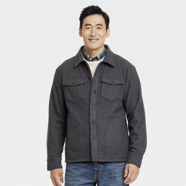 a man wearing a long sleeve shirt jacket over a sweater and collared shirt and denim jeans