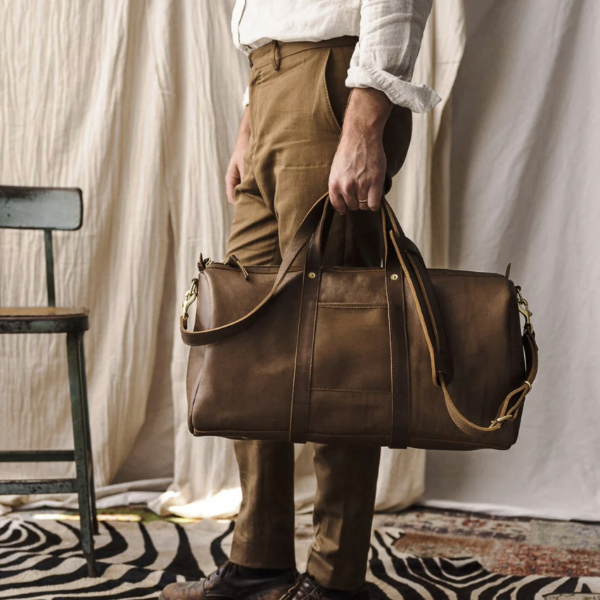 a man carrying a leather duffle weekender style bag
