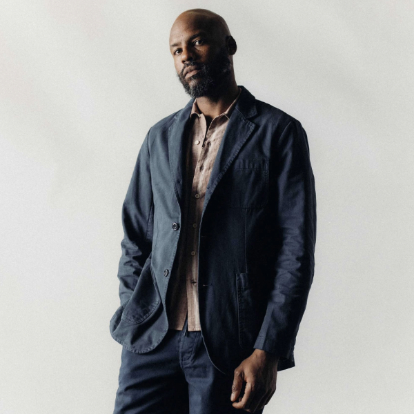 a man wearing a navy sportcoat over a collared shirt and pants